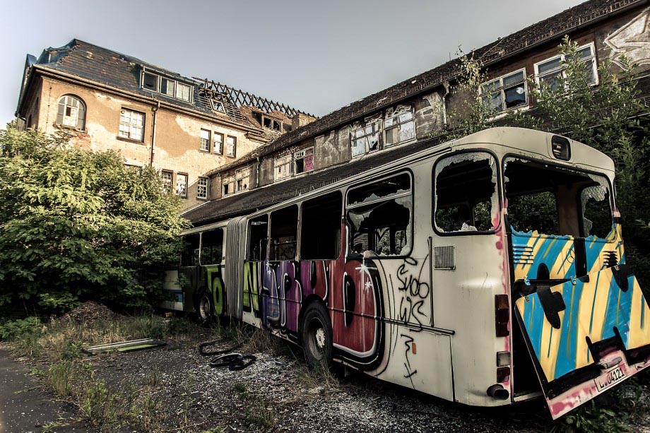 Ein verlassenes Fabrikgelände in Leipzig samt Bus in verfallenem Zustand. Ein im Weitwinkel aufgenommenes Foto - es ist viel auf dem Bild zu sehen, wirkt jedoch nicht überfrachtet, da ein inhaltlich sinnvoller Bezug zwischen Hauptmotiv (Bus) und "Hintergrund" (verlassenens Fabrikgelände) hergestellt wird.