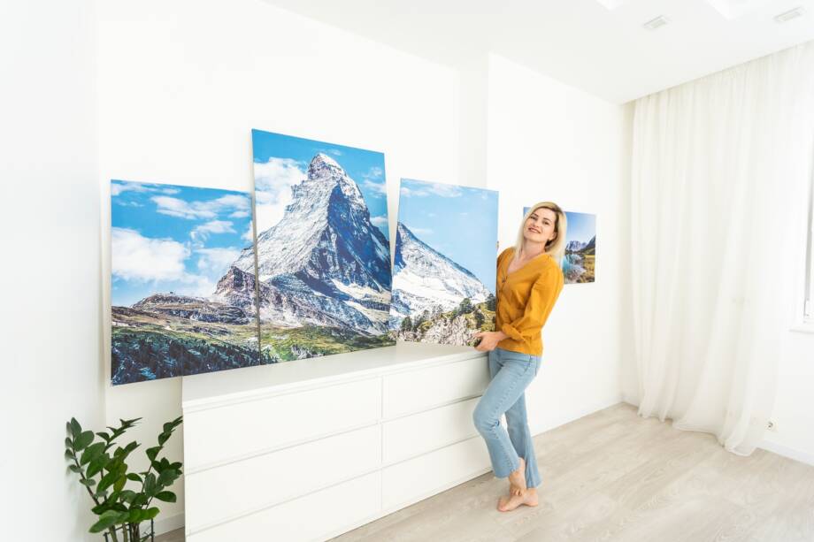 Leinwanddruck mit Galerieeinband. Frau hängt Fotografie an weißer Wand. Hände halten Foto Leinwanddruck.