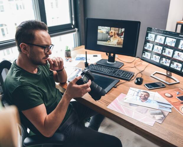 Gelassener bärtiger Fotograf schaut von oben auf die Kamera, während er sie im Büro in den Armen hält. Bildkonzept