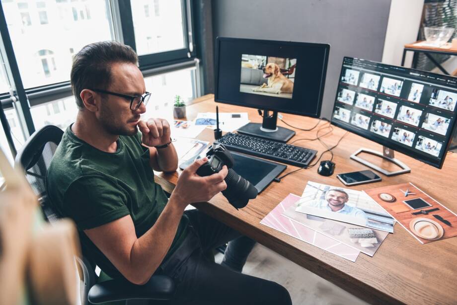 Gelassener bärtiger Fotograf schaut von oben auf die Kamera, während er sie im Büro in den Armen hält. Bildkonzept